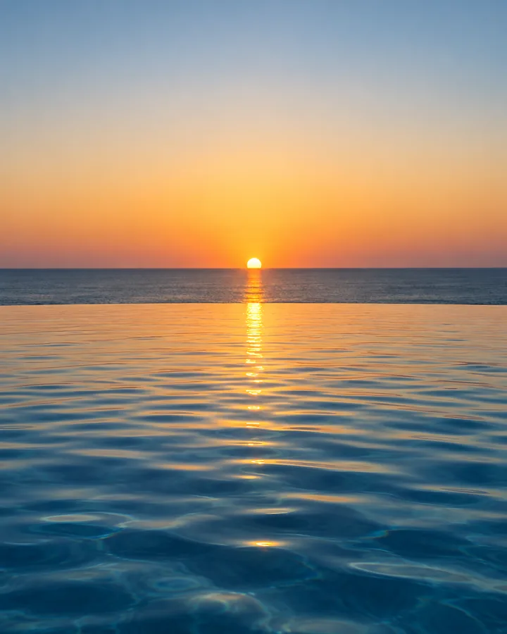 An infinity pool edge meeting the sea at sunset